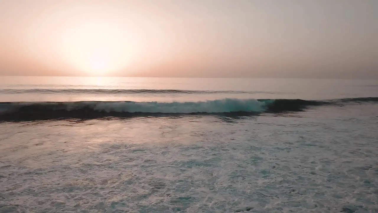 Slow panning shot of orange glowing sunset over sea with small breaking waves on rocky shore in foreground