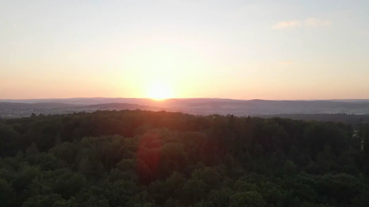 Fast-flying footage over a huge forest at an orange sunset and giving beautiful solar flares in the images with mountains in the background