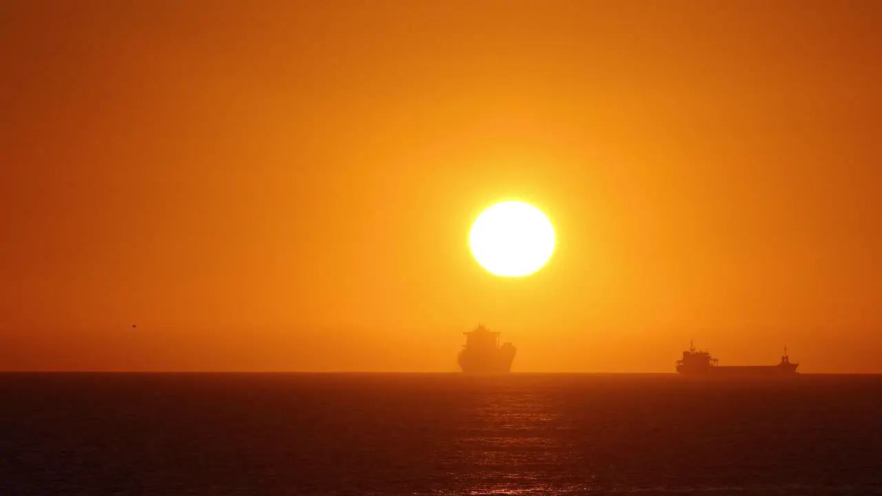 Time lapse of the sun setting over the ocean between two big ships in Europe