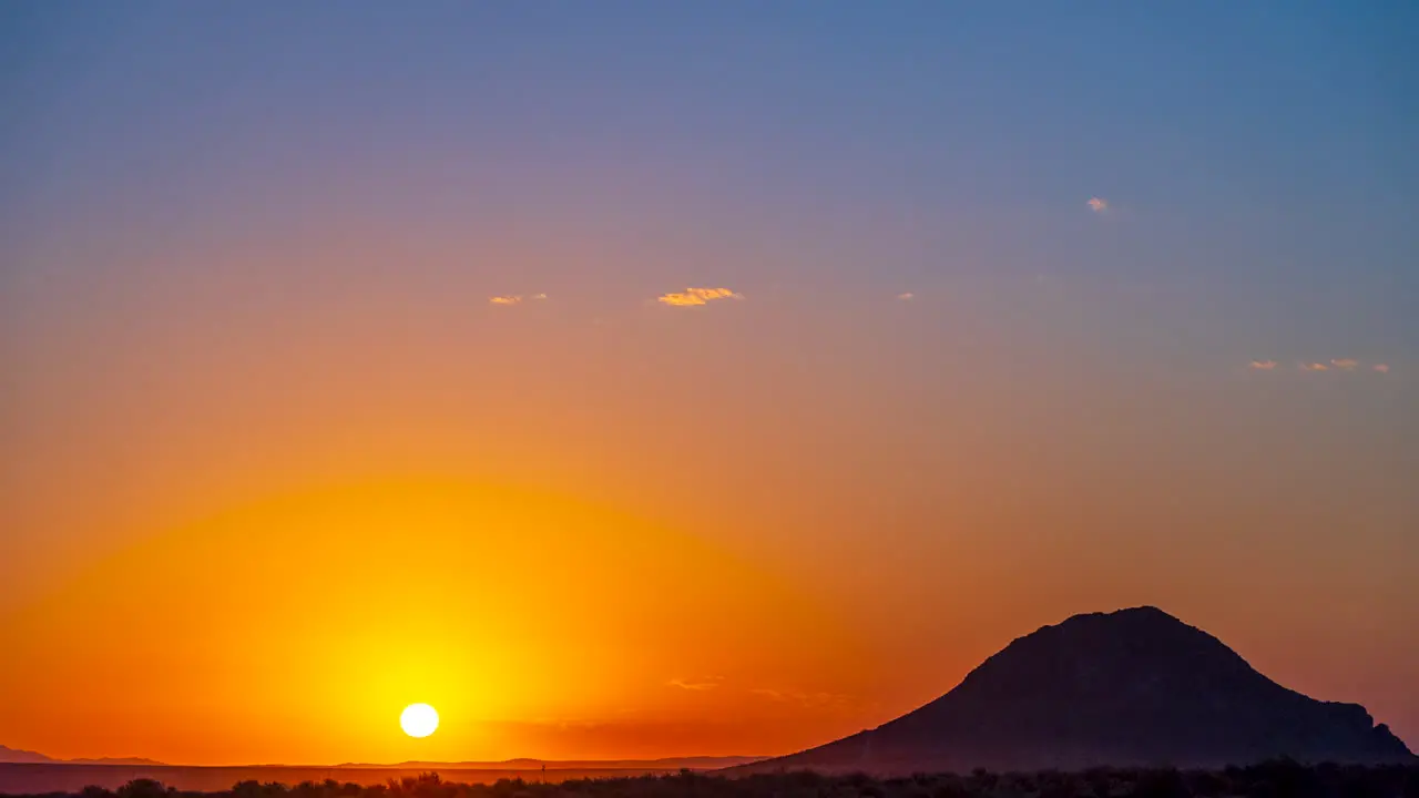 A fiery sunrise in the Mojave Desert landscape with a butte in silhouette time lapse