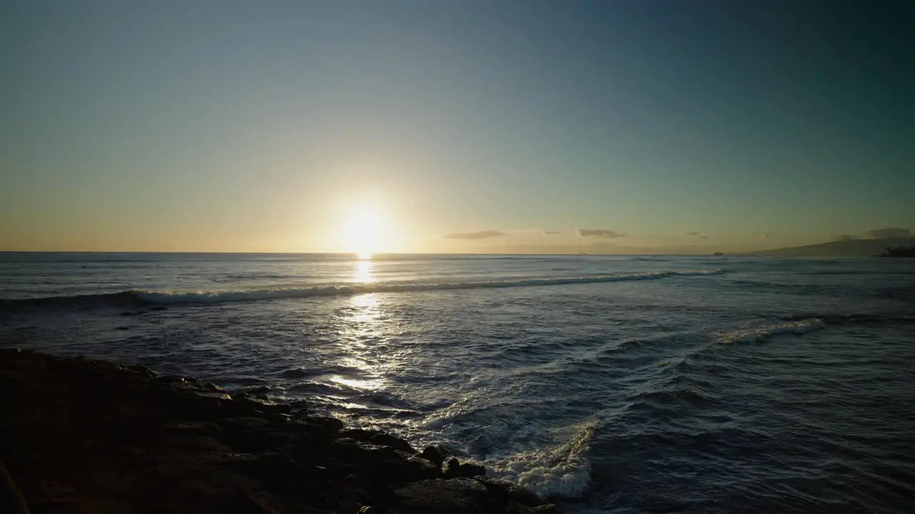 Hawaiian sunset with paddle boarder paddling into frame through waves