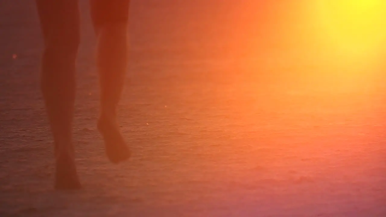 Slow Motion shot of girls running through sand kicking it up in the air with the glow of the sunset reflecting in the sand