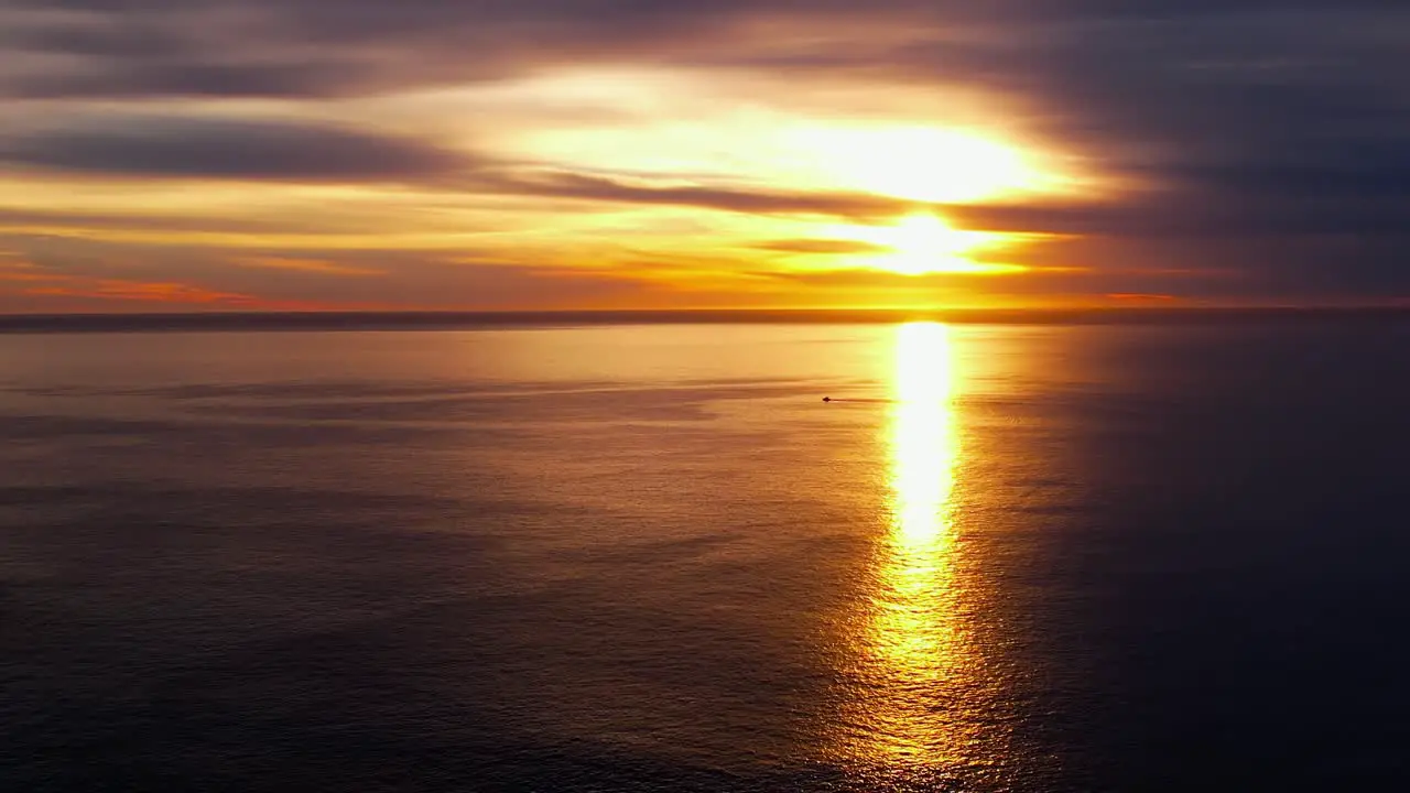 Golden sunrise over the Eastern horizon reflecting off the surface of the tranquil ocean descending aerial view