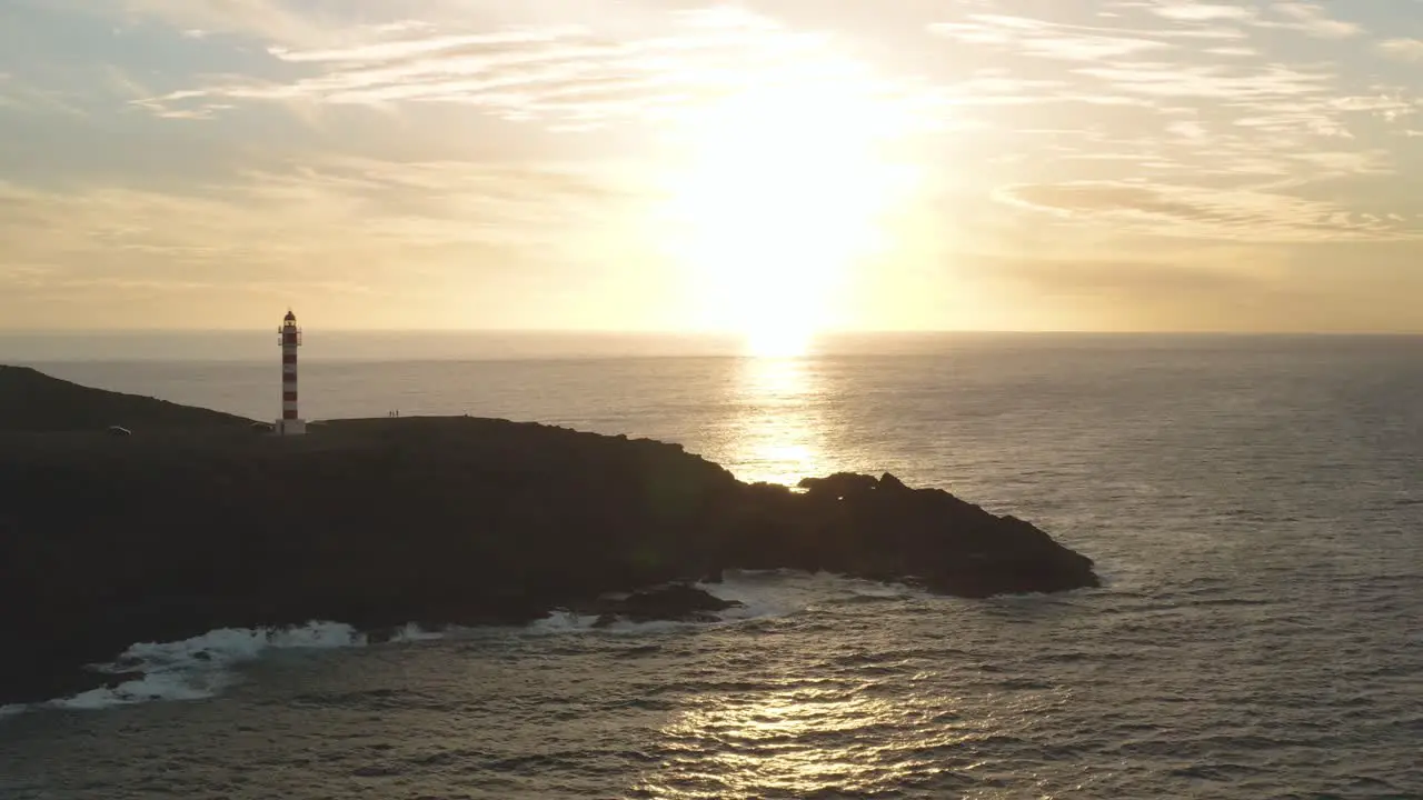 Panorama drone shot of a lighthouse at golden hour with ocean and sun