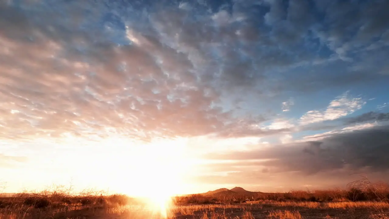 The sun rises in vibrant colors and shines over the desert landscape in this time lapse cloudscape