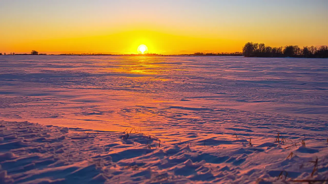 Bright yellow sunset time lapse over a field of snow dusk falls on the wide angle winter scene