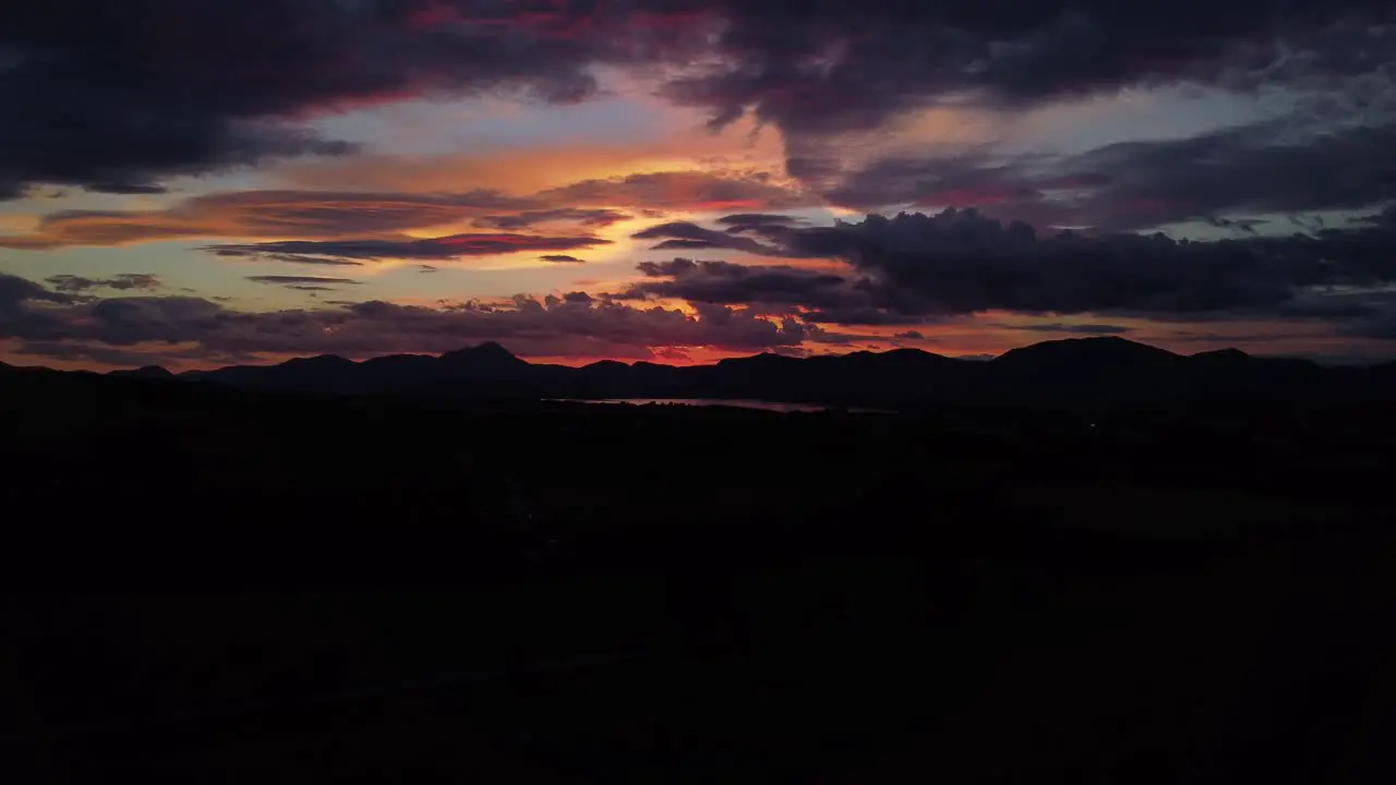 Drone shot of late sunset over fields and mountains with dramatic sky