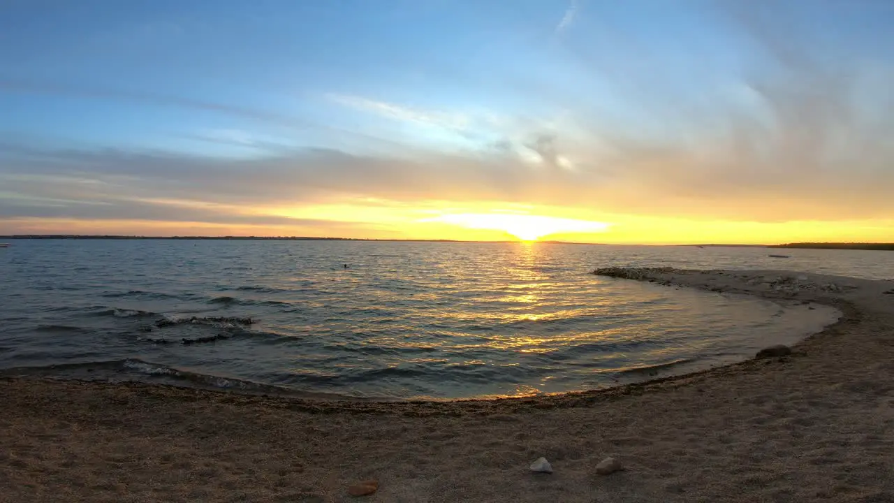 Empty pebble beach in sunset time lapse with waves and light clouds