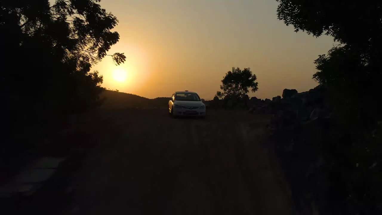 Drone rising upwards and forwards past a Honda civic car to reveal vast openness with a sunset