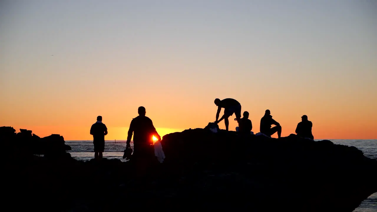 People watching sunset from rocks on beach silhouette