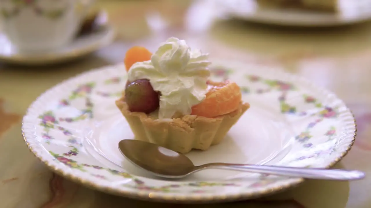 Biscuit fruit with cream on top as a dessert to a coffe break served on old fashioned plate with a spoon slow motion