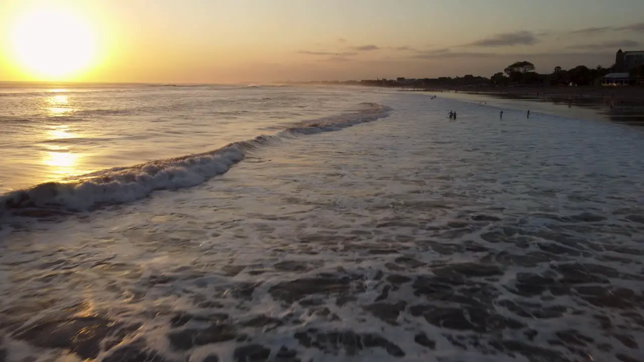 AERIAL Drone shot of a beach at sunset with people swimming in the ocean