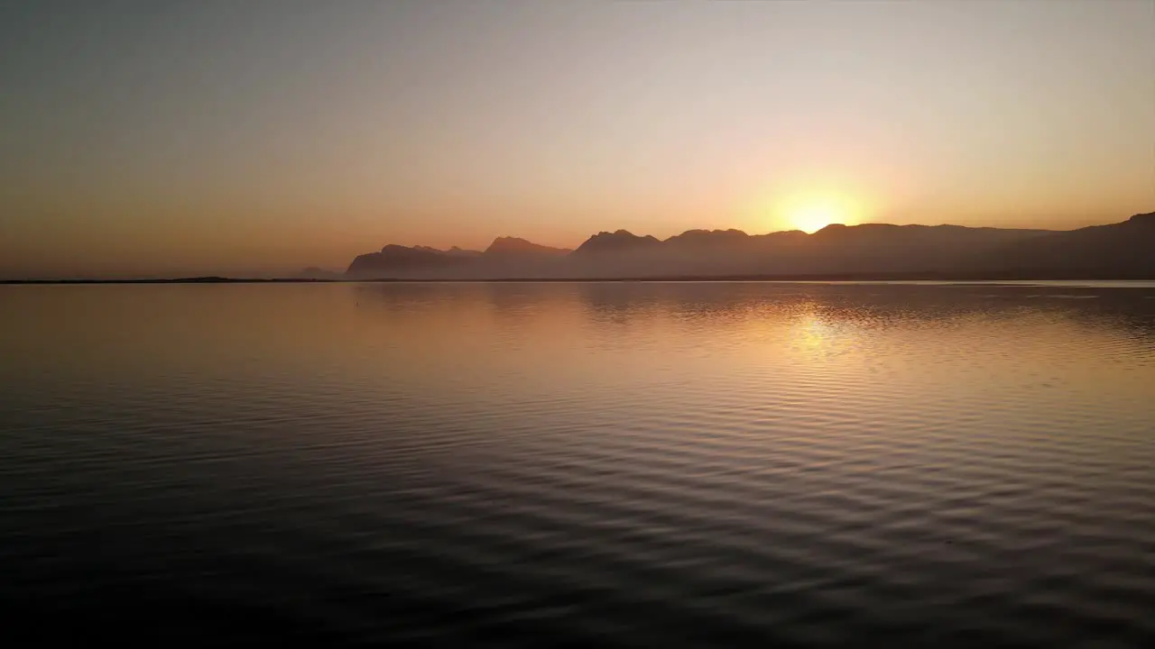 Peaceful scene of water ripples on a lagoon as the sun sets with mountains in the distance