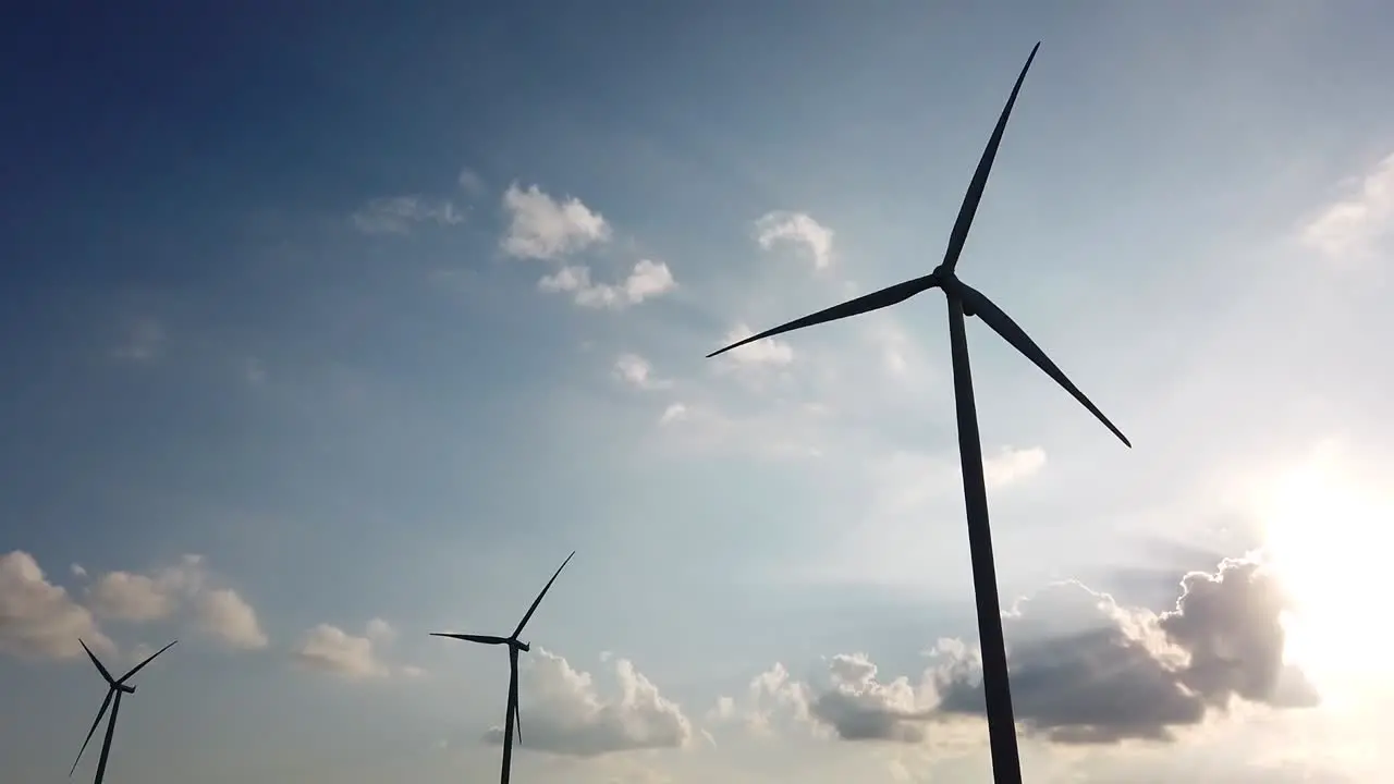 Three windturbines spinning in silhouettes in the afternoon while clouds are moving towards the horizon and the sky is blue