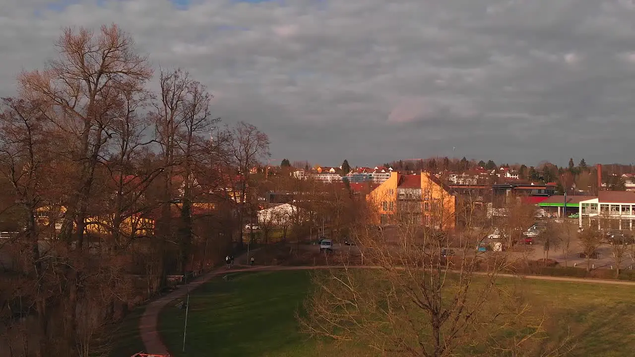 drone takes off in a park and there is a bridge nearby background buildings on sunset cloudy sky