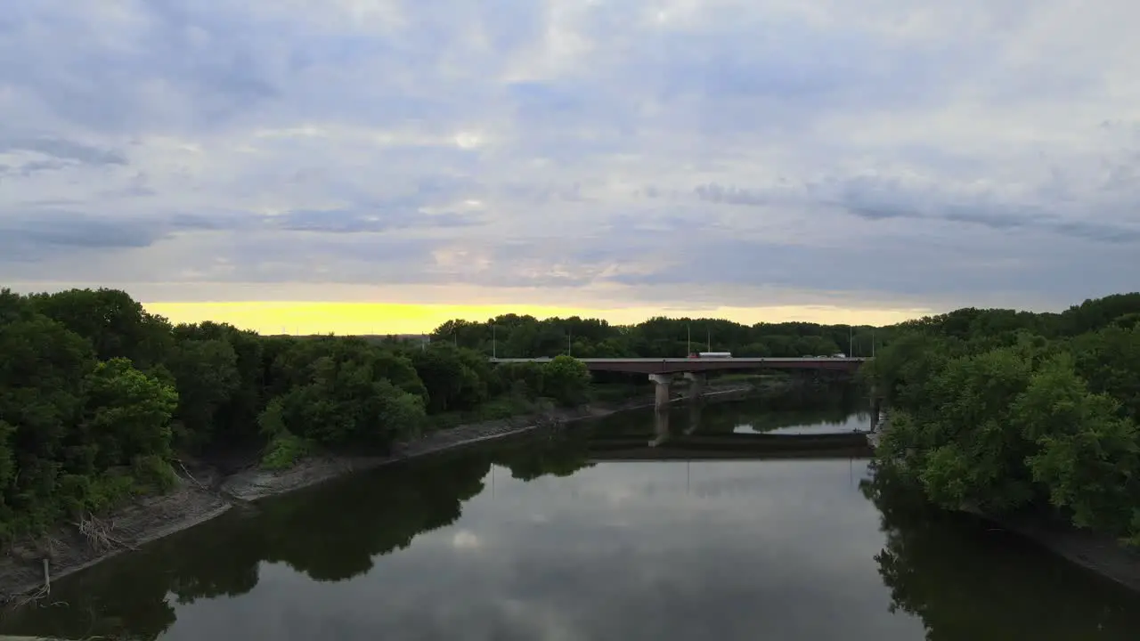 As the sunsets over the highway bridge crossing a river that feeds the Mississippi south of the Twin Cities in Minnesota the shoreline reflects off of the Stillwater