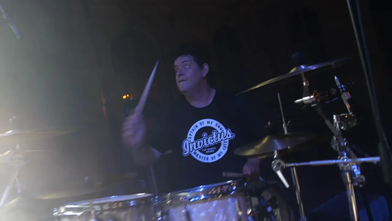 A drummer playing on stage seen through smoke and lights