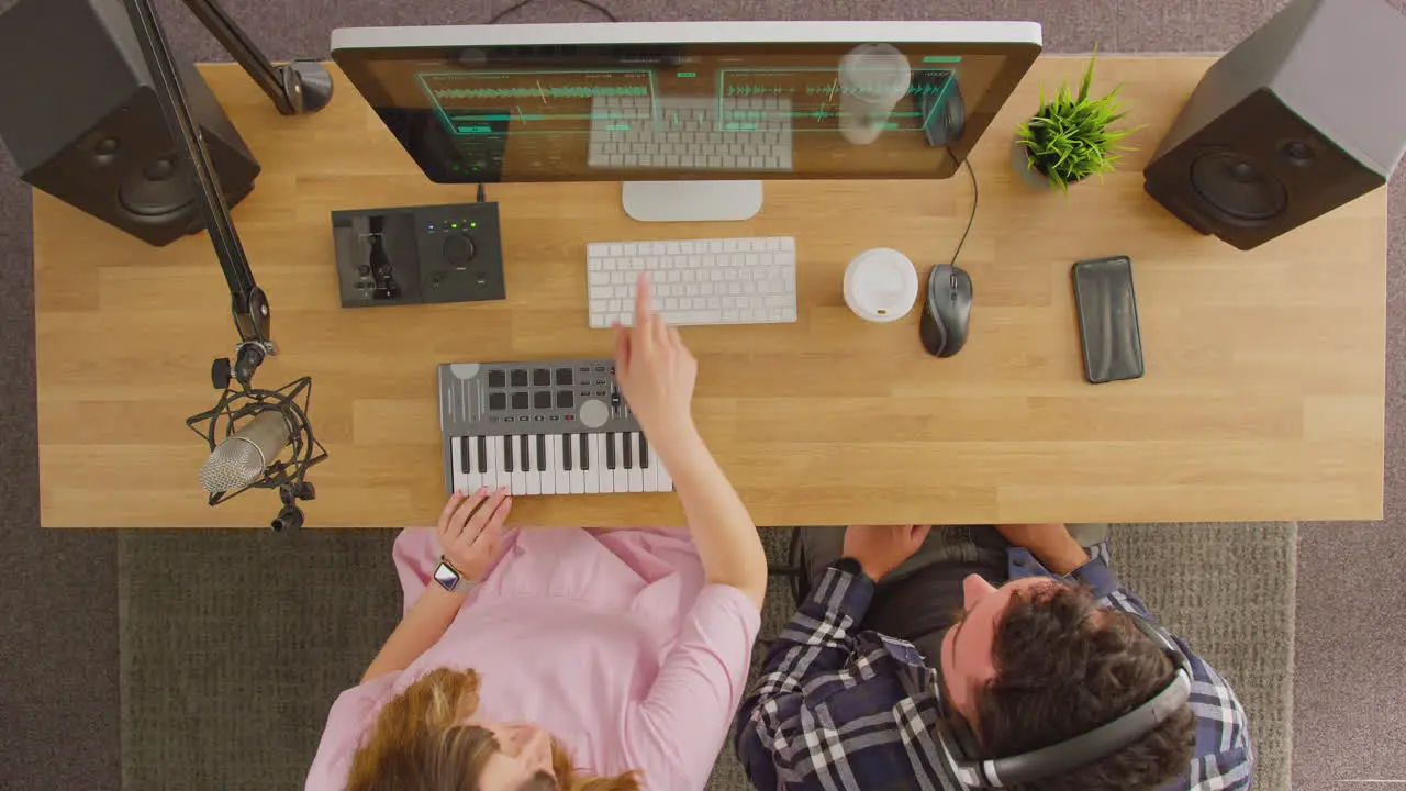 Overhead View Of Male And Female Musicians At Workstation With Keyboard And Microphone In Studio