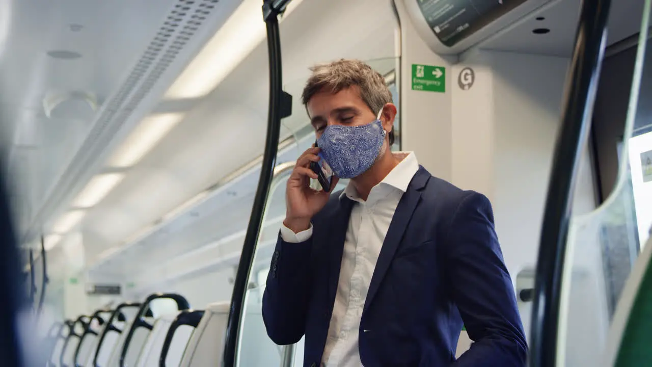 Businessman Stands In Train Carriage Talking On Mobile Phone Wearing PPE Face Masks During Pandemic