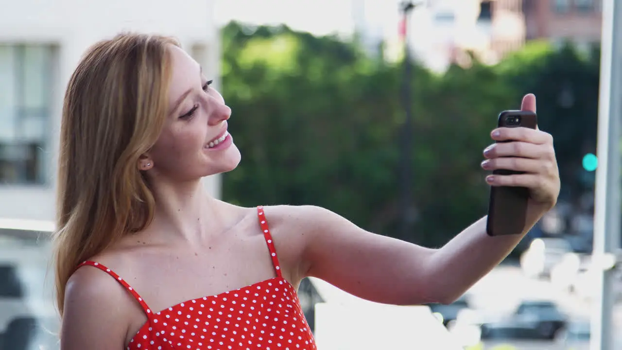 Young Businesswoman Having Video Chat On Mobile Phone Standing Outside City Office Building