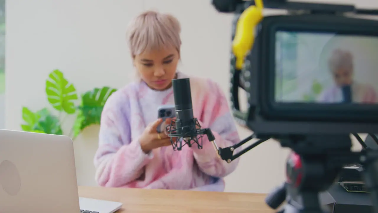 View Through Camera Of Female Vlogger Looking At Mobile Phone Before Live Stream