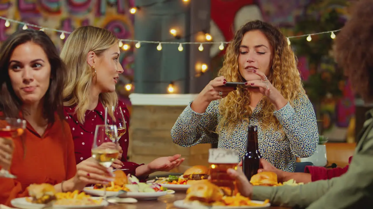 Woman Taking Photo Of Food As Multi-Cultural Group Of Friends Enjoy Night Out In Restaurant Together