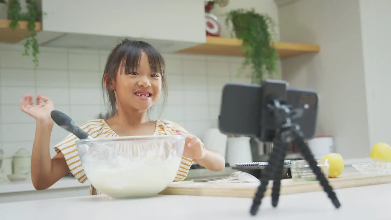 Asian Girl Baking Cupcakes In Kitchen At Home Whilst Vlogging On Mobile Phone