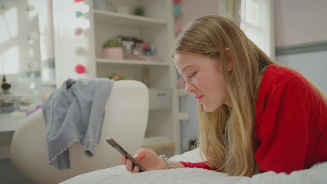 Teenage girl wearing orthodontic braces lying on bed at home using mobile phone and smiling shot in slow motion