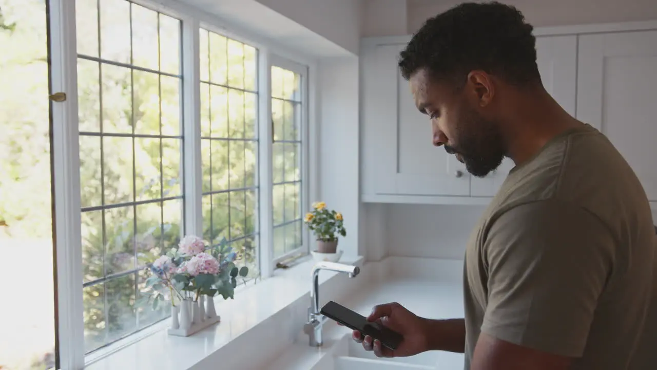 Close Up Of American Male Soldier In Uniform In Kitchen On Home Leave With Mobile Phone