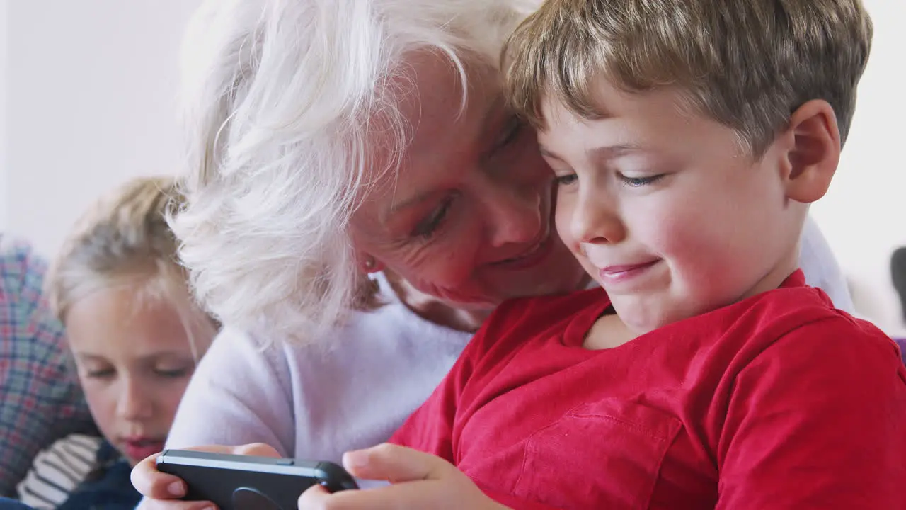 Grandmother Playing Video Game With Grandson On Mobile Phone At Home