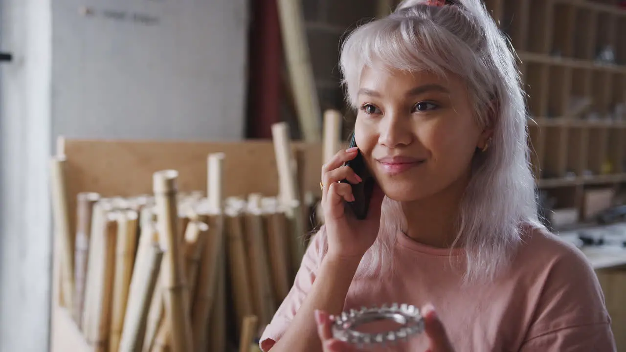 Female Business Owner In Workshop Making Call On Mobile Phone To Discuss Component