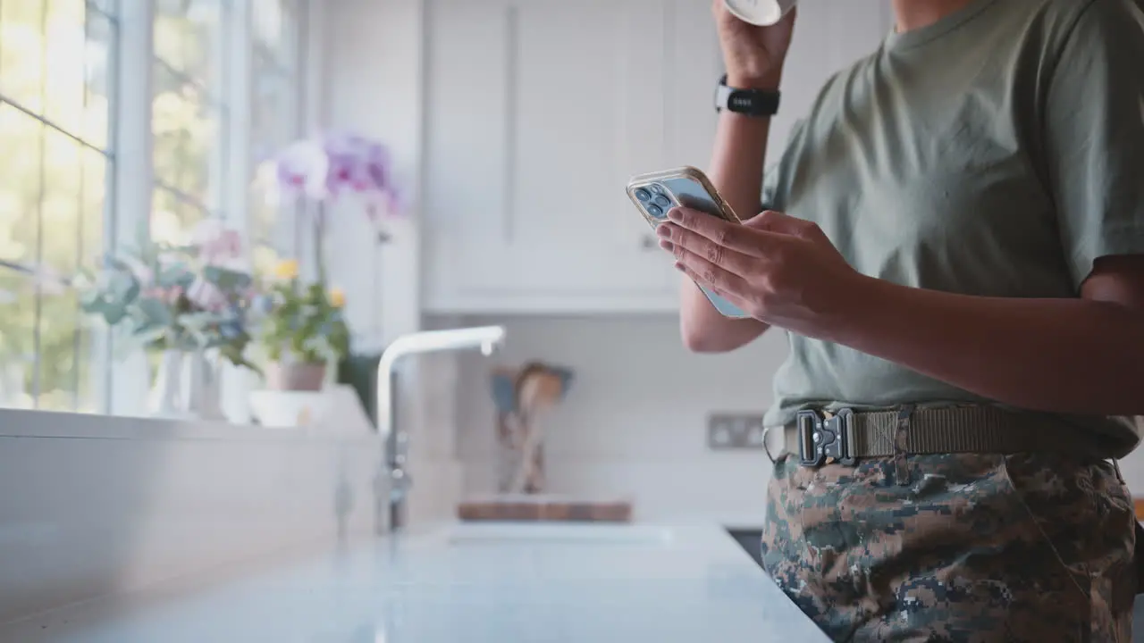 Close Up Of American Female Soldier In Uniform In Kitchen On Home Leave With Mobile Phone