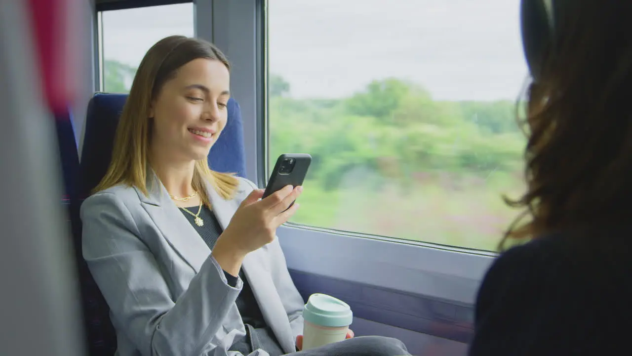 Businesswoman With Takeaway Coffee Commuting To Work On Train Looking At Mobile Phone