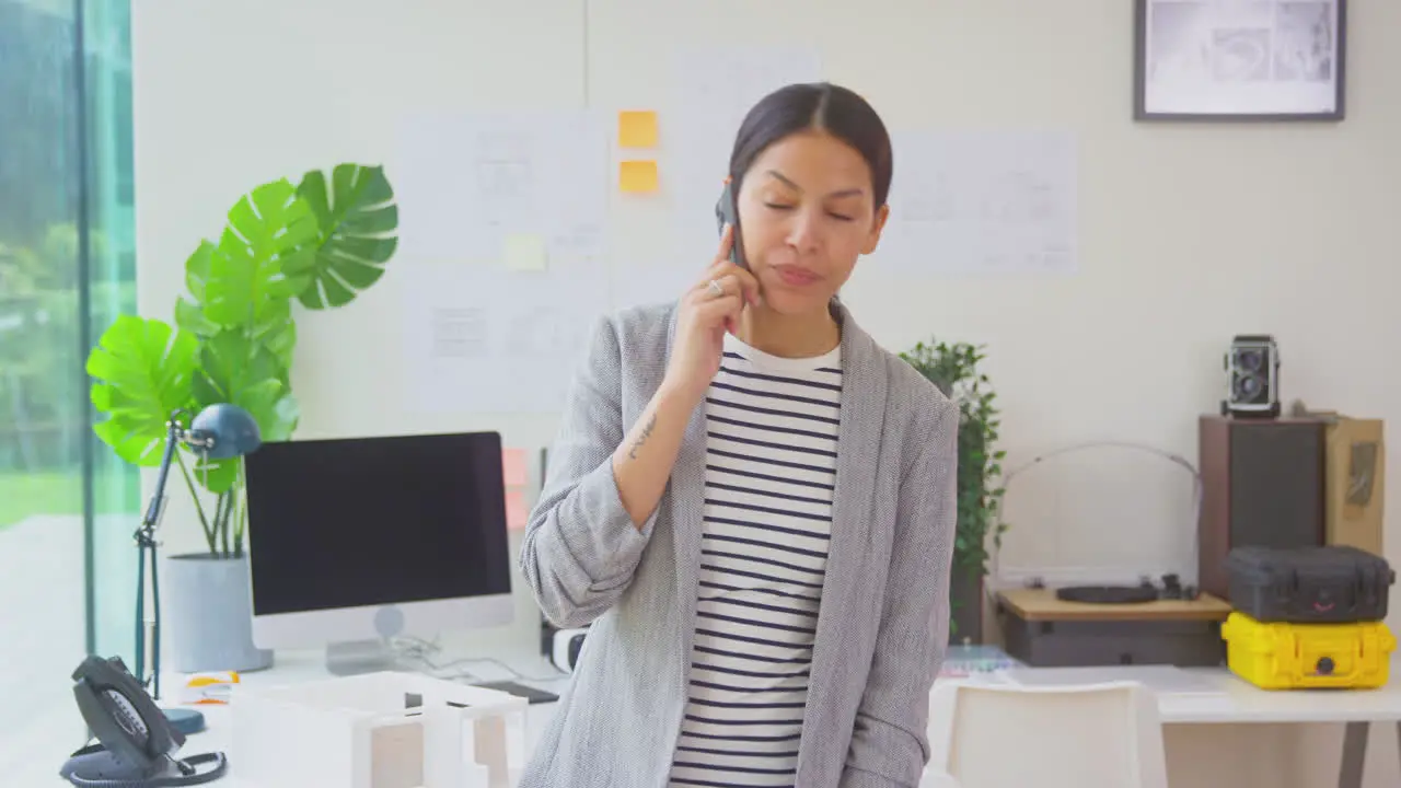 Female Architect Working In Office Standing At Desk Talking On Mobile Phone