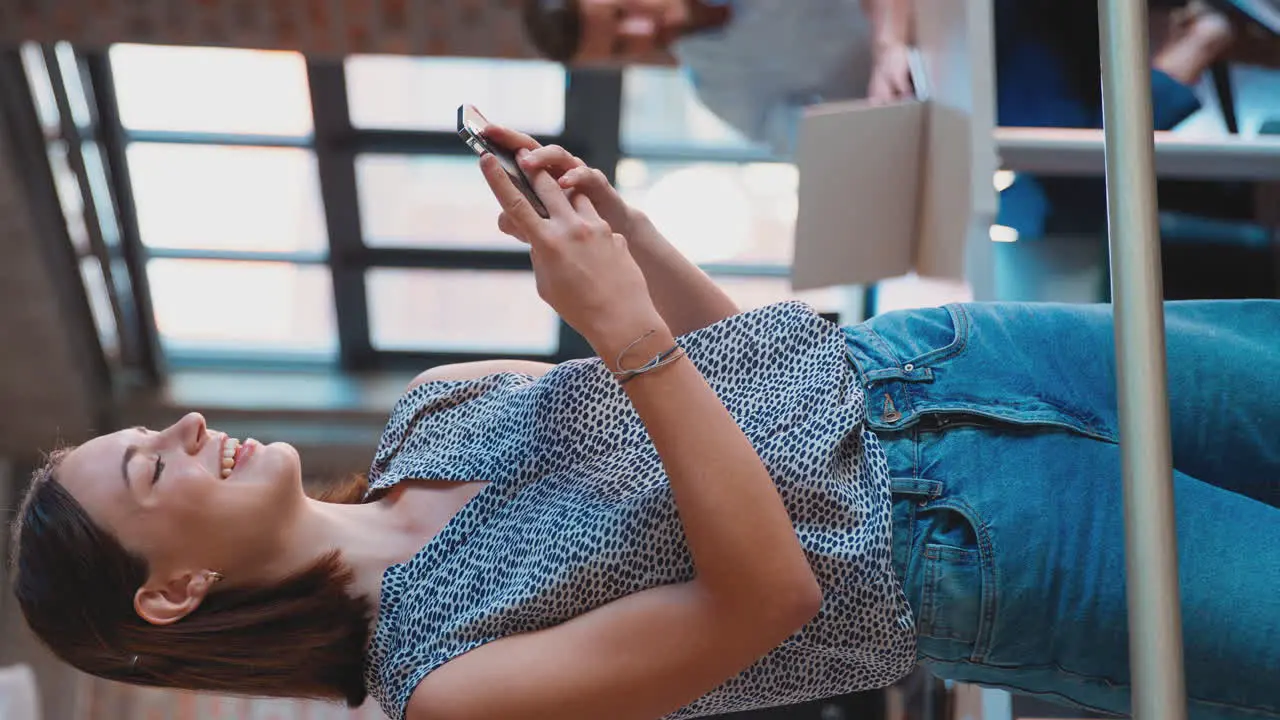 Vertical Video Of Smiling Businesswoman Standing In Busy Office Messaging On Mobile Phone