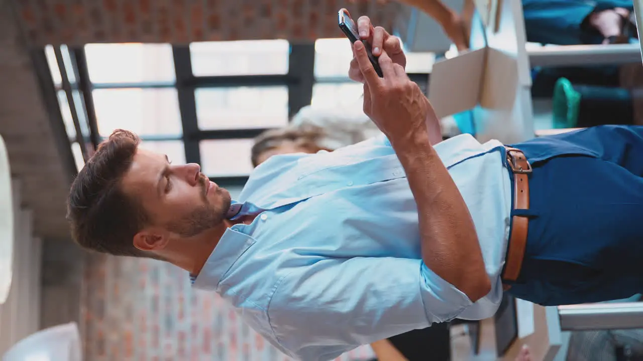 Vertical Video Of Businessman Standing In Busy Office Messaging On Mobile Phone