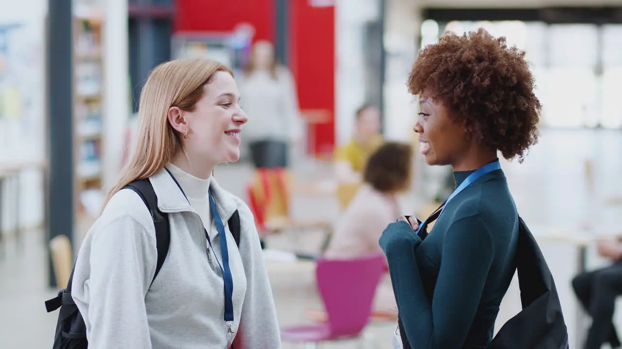 Two Female College Student Friends Meeting And Looking At Mobile Phone In Communal Campus Building