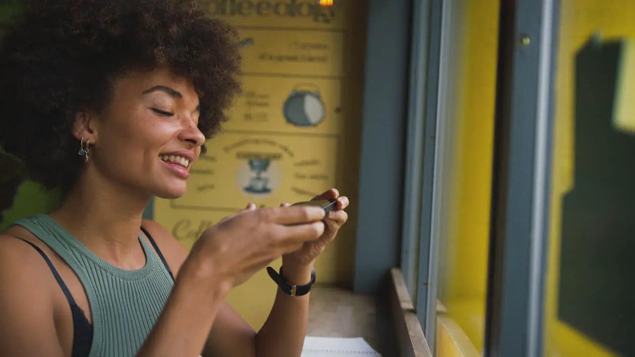 Woman In Coffee Shop Taking Picture Of Food To Post On Social Media