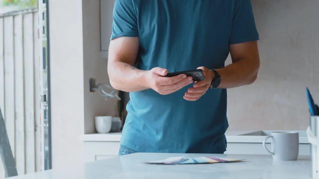 Man Renovating Kitchen At Home Taking Picture Of Paint Colour Swatches On Mobile Phone