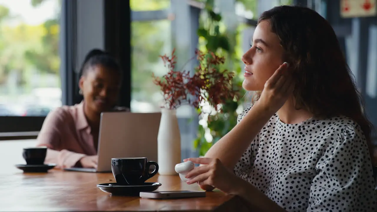 Businesswoman With Mobile Phone Putting In Wireless Earbuds Working In Coffee Shop