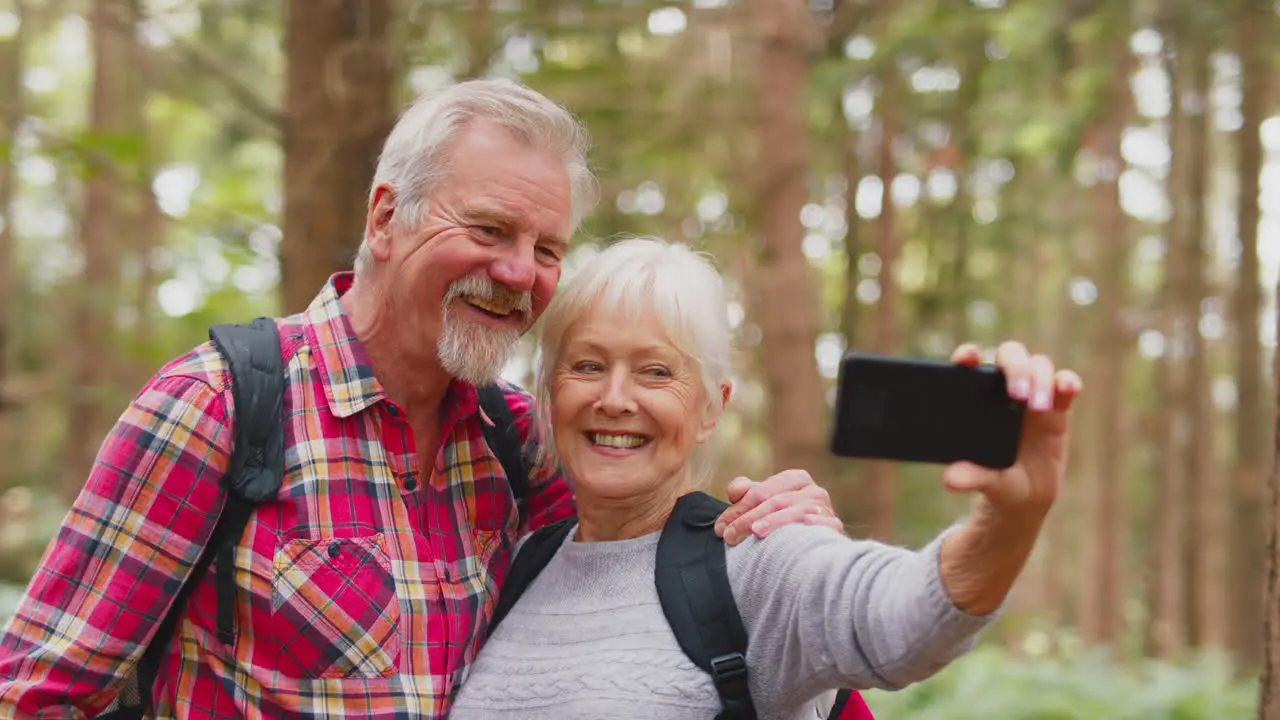 Retired Senior Couple Posing For Selfie On Mobile Phone Hiking In Woodland Countryside