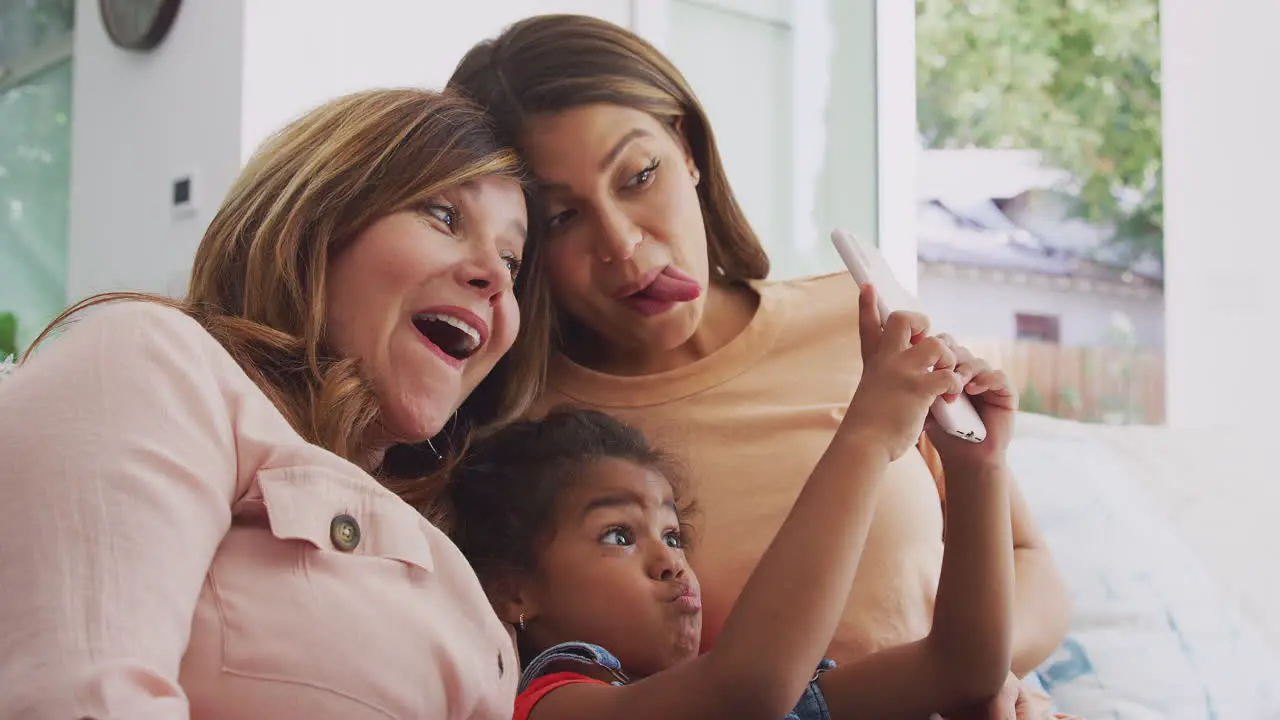 Multi-Generation Female Hispanic Family At Home Pulling Funny Faces For Selfie On Mobile Phone