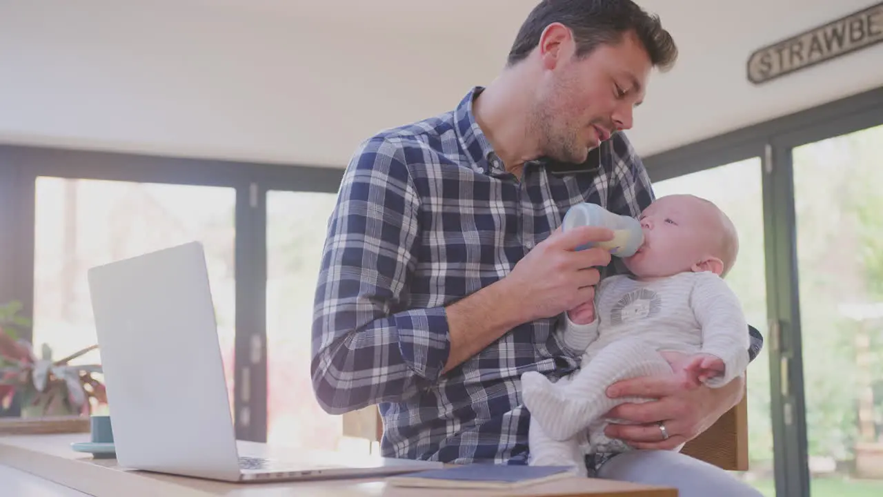 Working father multi-tasking talking on mobile phone whilst feeding crying baby son with bottle shot in slow motion