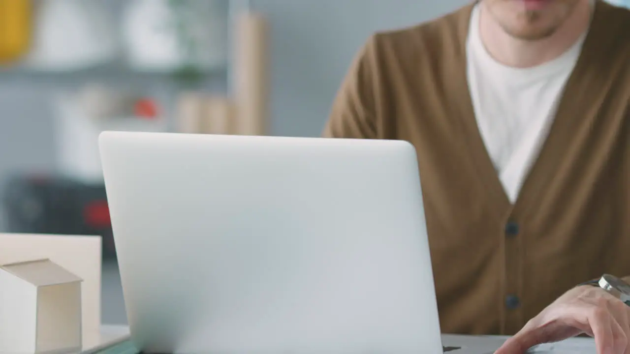 Male Architect In Office Working At Desk On Laptop Taking Speakerphone Call On Mobile Phone