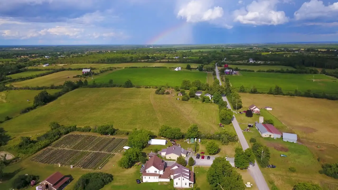 Aerial rise over a farm with a rainbow and storm clouds in the distance