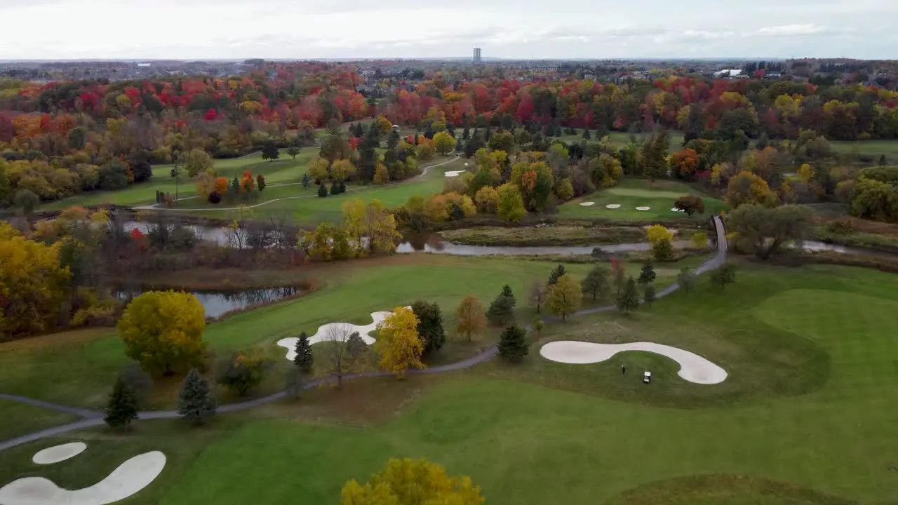 Fly over a golf course surrounded by a park in a fall cloudy moody day