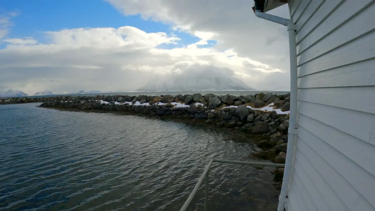 POV shot walking along the harbor building over looking the breakwater and revealing the sea clouds and snow covered mountains Åse Harbor Andoya Norway