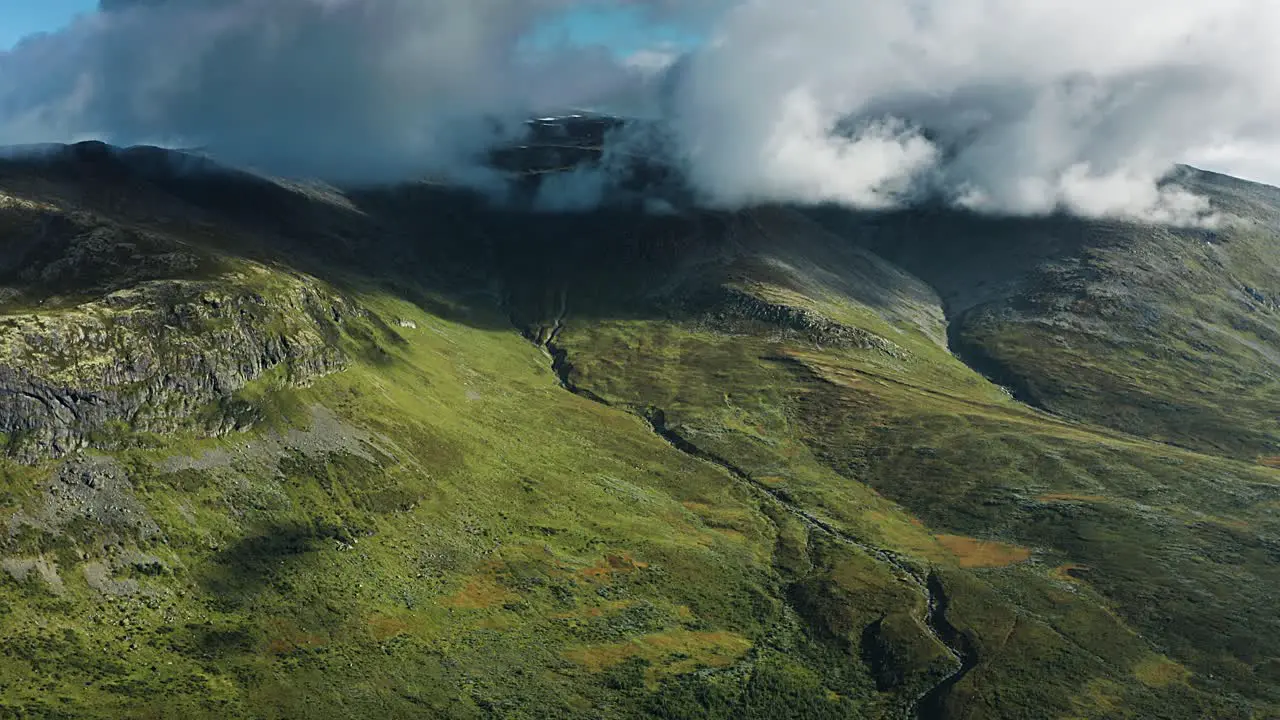 Fast flight pan shot of dense white clouds whirling above the green hills of Norwegian Aurlandsfjellet