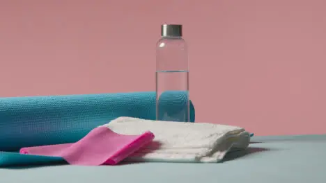 Fitness Studio Shot Of Water Bottle With Exercise Mat And Towel Against Pink Background