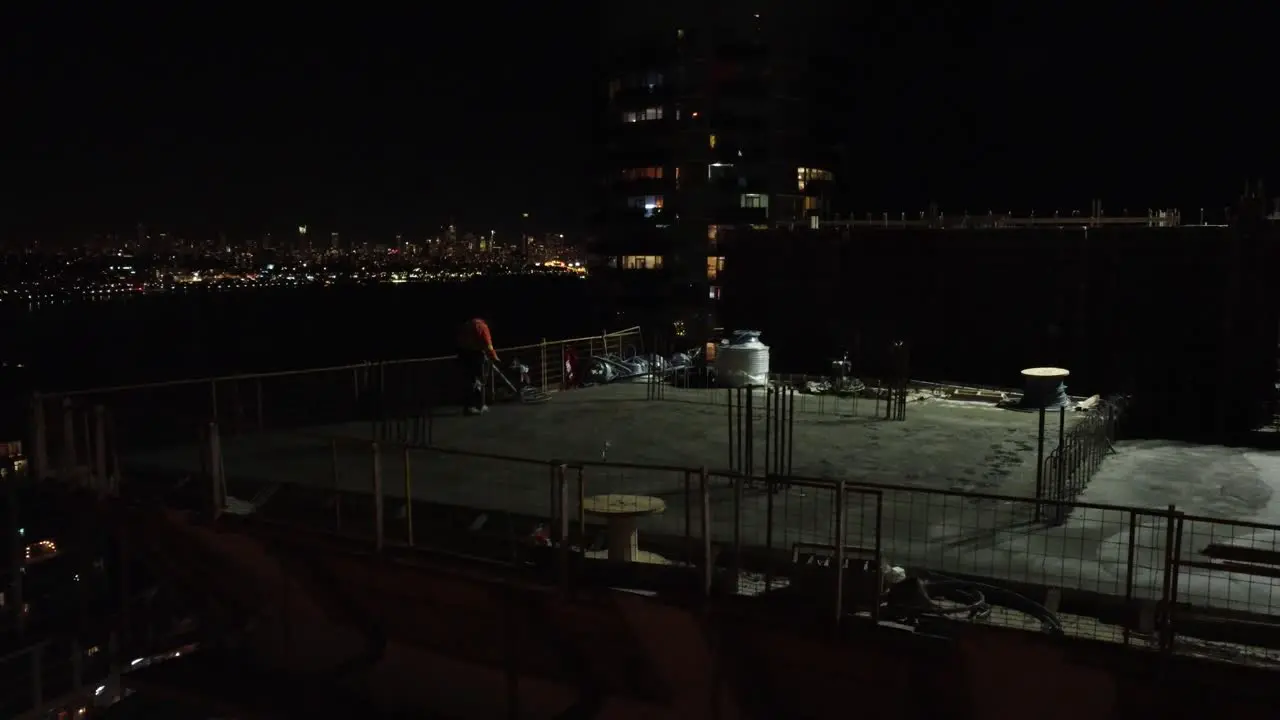 Aerial footage of a worker building a skyscraper at night with the help of a crane capturing the beauty of urban construction